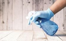 Hand with glove using cleaning spray bottle on wooden surface