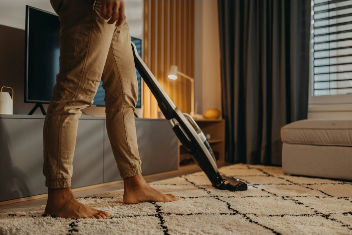 A person vacuuming a patterned rug in a cosy living room.